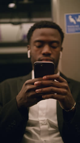 Vertical-Video-Of-Young-Businessman-In-Suit-Commuting-To-Work-Sitting-In-London-Underground-Tube-Train-Wearing-Wireless-Earbuds-To-Stream-From-Mobile-Phone-Shot-In-Real-Time-4